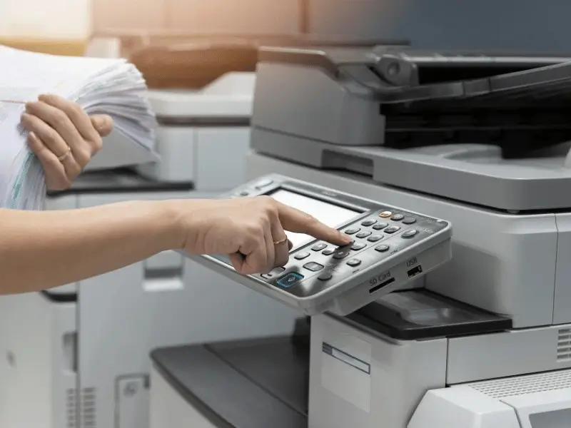Businesswoman operating office copier amidst stacks of paperwork in office